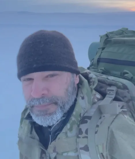 A bearded tester in MultiCam with frost in his beard, carrying a Lightning Pack across snow at dusk in the Arctic Circle.